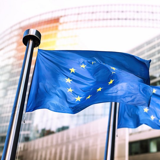 Zwei wehende Europa-Flaggen vor Bürogebäuden.