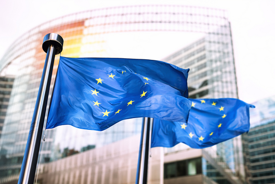 Zwei wehende Europaflaggen vor einem Bürokomplex.