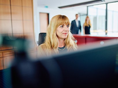 Eine Frau sitzt hinter dem Bildschirm im Hintergrund laufen Personen vorbei