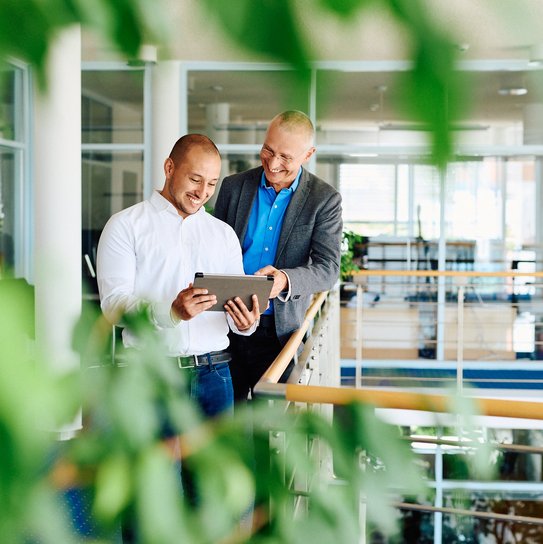 Zwei Mitarbeitende stehen in einem modernen Büro und betrachten gemeinsam ein Tablet.