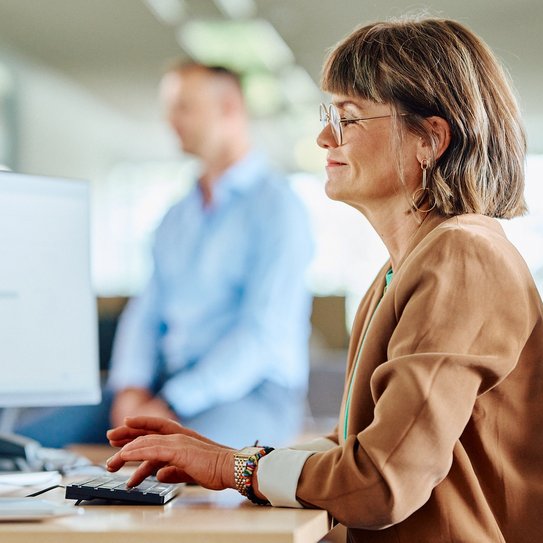 Eine Mitarbeitende sitzt lächelnd an ihrem Arbeitsplatz und betrachtet ihren Bildschirm.