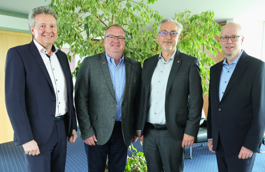 Eine Gruppe aus vier Männer welche nebeneinander stehen und in die Kamera schauen