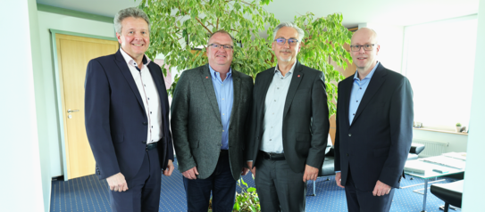 Eine Gruppe aus vier Männer welche nebeneinander stehen und in die Kamera schauen