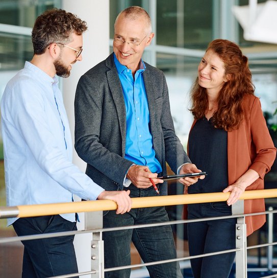 Drei Personen stehen in einem Büroflur und tauschen sich über eine Idee aus.